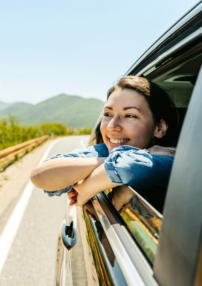 Woman smiling and looking out the window of moving car as it drives down the highway